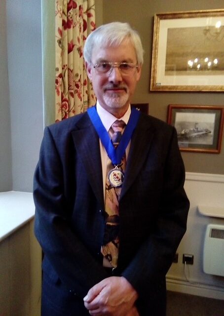 Bob Merrett in suit with medal around his neck