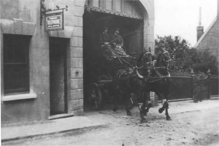 Pair of horses pulling cart with two men atop.