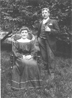 Woman in chair and man standing with pipe